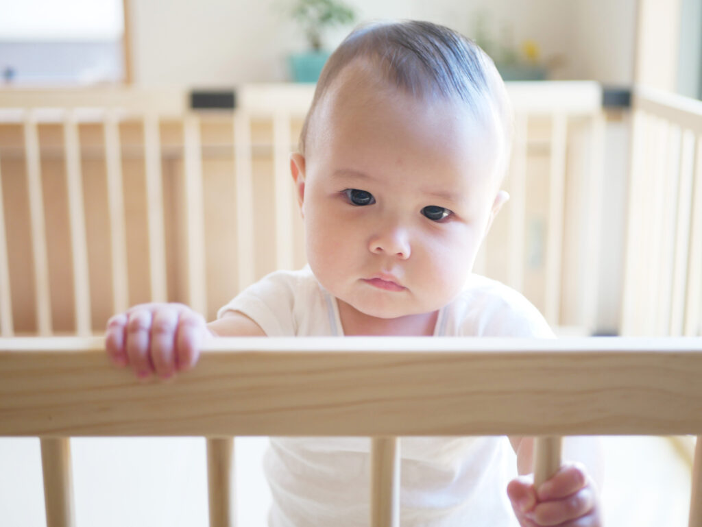 A,Baby,Holds,A,Playpen,And,Looks,At,Camera